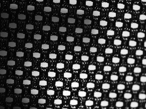 Macro close-up of black open mesh fabric with geometric grid pattern and backlighting, creating an abstract textile texture for fashion, design and background concepts.
