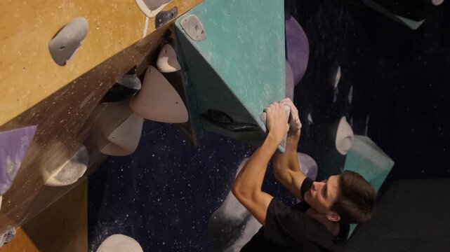 Young man jumps up grabbing ledge on wall slow motion. Seasoned athlete begins to overcome height in rock climbing center