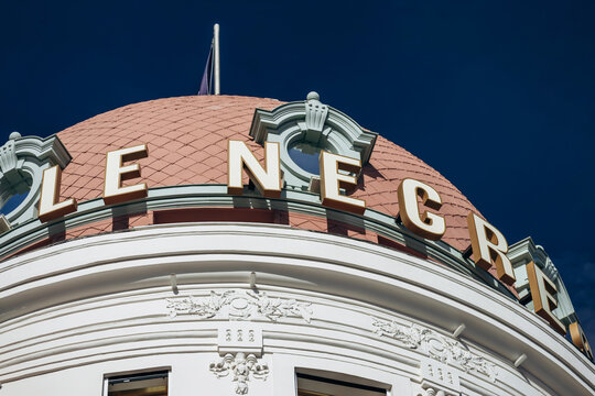 Nice, France - November 11, 2025: Pink dome, rooftop lettering and ornate white facade of Hotel Negresco against a clear blue sky.