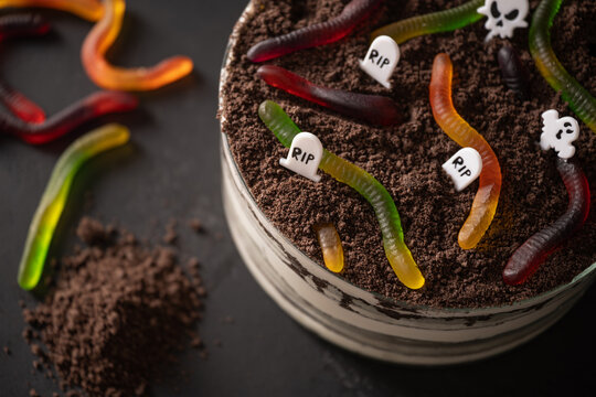 Close up of Halloween graveyard Dirt cake topped with chocolate crumbs, gummy worms and RIP tombstones. Creepy homemade dessert for spooky party.