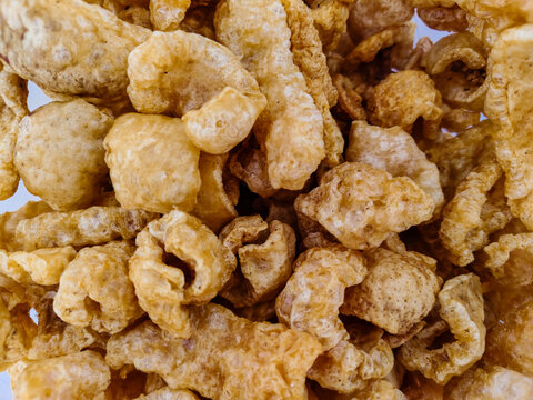 Detailed close-up shot of crispy, golden-brown fried pork rinds. Delicious savory snack (chicharr&oacute;n). Irregular, puffed texture, appetizingly crunchy.
