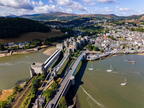 Drone perspective of historic fortified castle and suspension bridge, yachts moored in estuary below stone battlements, a preserved heritage site