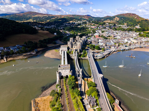 Drone shot of medieval fortress of Conwy and Thomas Telford suspension bridge, showing stone towers and railway line leading into the castle walls.