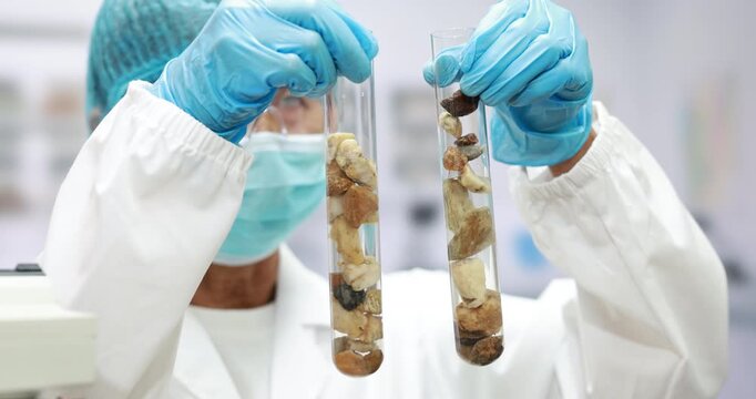 Scientist in protective clothing holds two test tubes filled with soil and rock samples in a laboratory.