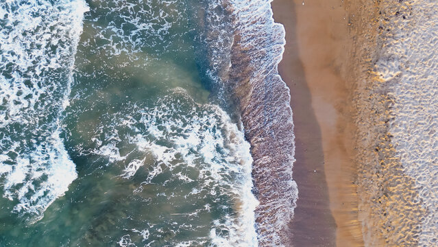 Top down aerial perspective of ocean surf hitting sandy coastline creating vivid water texture and right side copy space area for tropical summer travel design