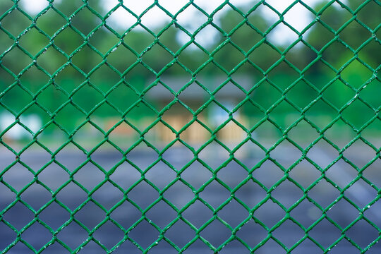 Green chain link fence texture close up with blurred sports ground in background. Outdoor security barrier, metal mesh netting, property protection and safety boundary concept.