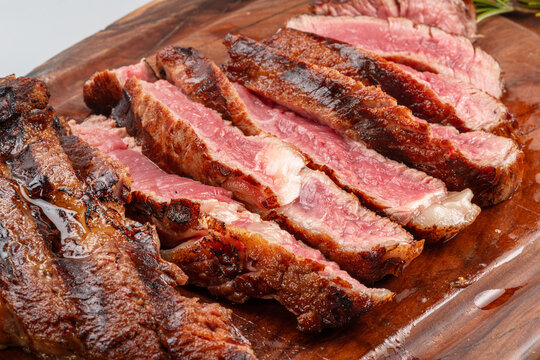 Sliced grilled beef ribeye steak medium rare on wooden cutting board