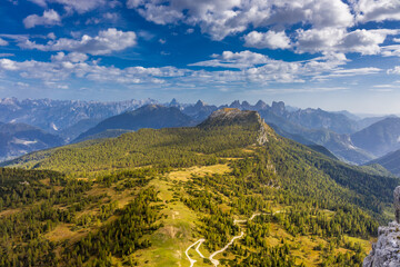 Fototapeta premium Dramatic Dolomites mountain landscape in northern Italy, featuring rugged limestone peaks, green alpine meadows, forested slopes, and a clear mountain atmosphere. A scenic natural destination