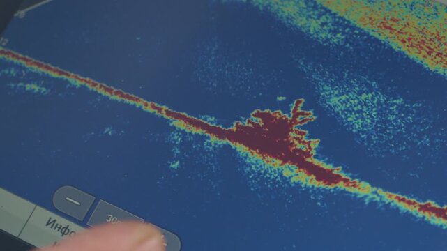Angler searches for fish with the fish finder. Display of the fish finder with the real time image of the bottom of the lake filled with wooden logs, camera pans to the angler afterwards