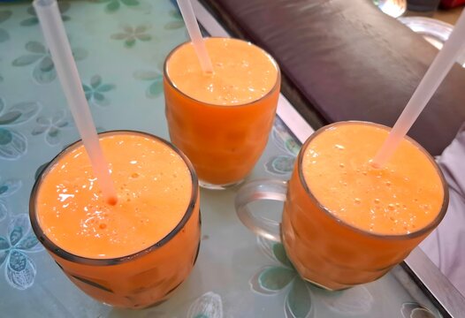 Three glasses of fresh mango juice with straws on a patterned table
