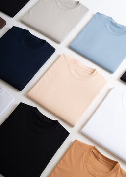 A clean flat lay composition of neatly folded plain t-shirts in various solid colors on a white background.