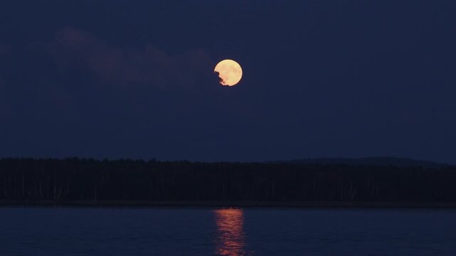 Full Moon appears from the clouds during moonrise on the river