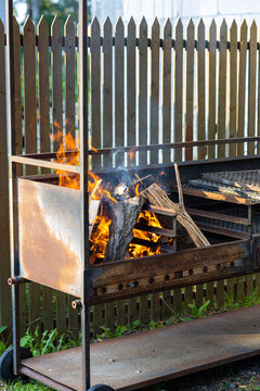 Burning Firewood in a Metal Garden Grill. Firewood burning with bright flames inside a metal outdoor grill in a residential garden. Several pieces of split wood are arranged on the grill grate
