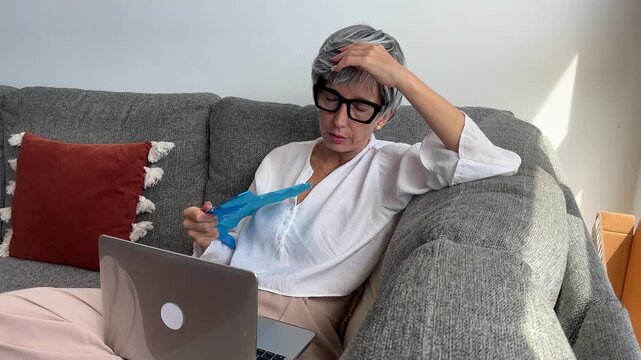 Mujer con sofocos abanic&aacute;ndose en sof&aacute; y trabajando con laptop