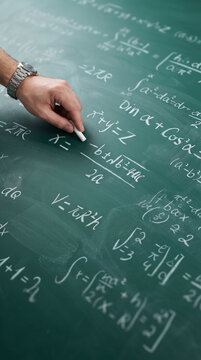 Teacher hand writing complex mathematical quadratic formulas and calculus theorems with white chalk on green chalkboard illustrating academic classroom learning and school lectures