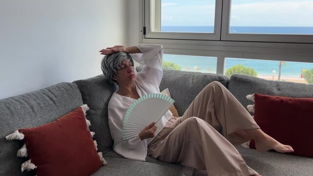 Mujer menop&aacute;usica caminando hacia el sof&aacute; y abanic&aacute;ndose