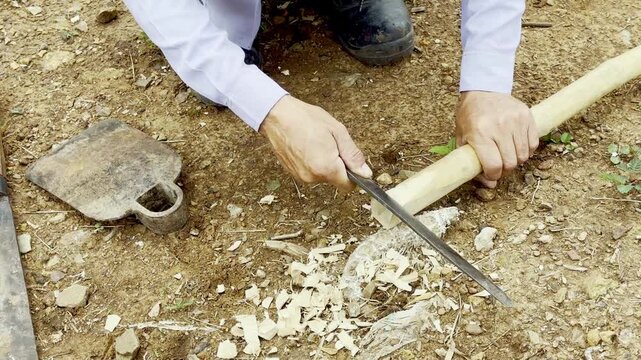 A Thai local craftsman uses a traditional Thai knife to carve bamboo for making a hoe handle, reflecting rural lifestyle and local craftsmanship.