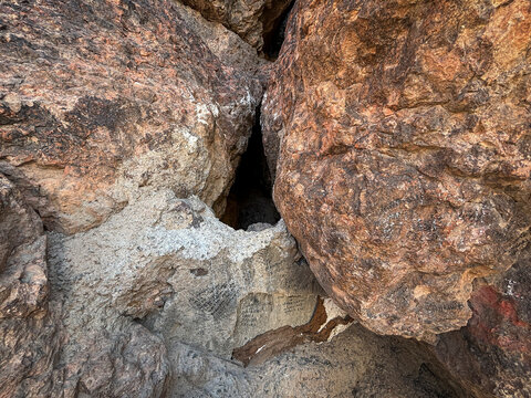 Sunlight and shadow fall across a narrow crevice between two large boulders marked with handwritten graffiti, Al Madinah Province, Madinah, Saudi Arabia