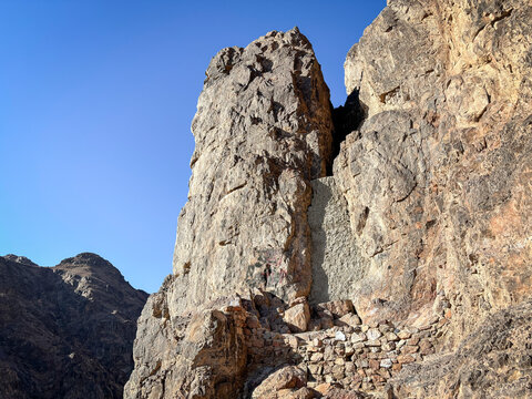A tall split boulder stands over a stone pathway on the rocky slope of the archers hill, Al Madinah Province, Madinah, Saudi Arabia