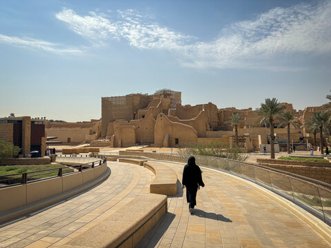 A woman walks along an elevated walkway toward the mud brick ruins of At-Turaif, Riyadh, Riyadh, Saudi Arabia