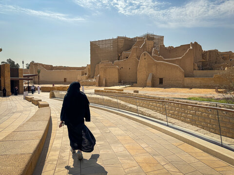 A woman walks alone across the stone plaza before the restored walls of At-Turaif, Riyadh, Riyadh, Saudi Arabia