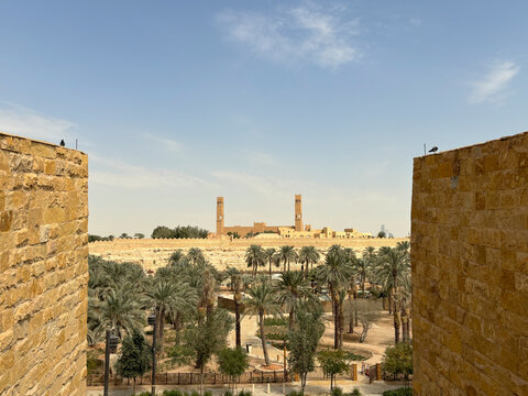Two crenellated mud brick towers frame a distant view of a towered building across the palm grove, Riyadh, Riyadh, Saudi Arabia