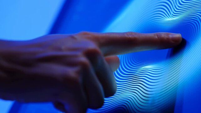 Close-up hand glides index finger across luminous blue digital surface while fine white wave lines bend around the touch point, creating fluid interactive motion and depth