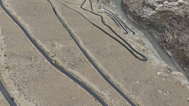 Aerial view of a dramatic mountain road with hairpin loops and zig-zag switchbacks carved into a barren slope above a river gorge in Spiti Valley Himachal Pradesh India shot by a drone