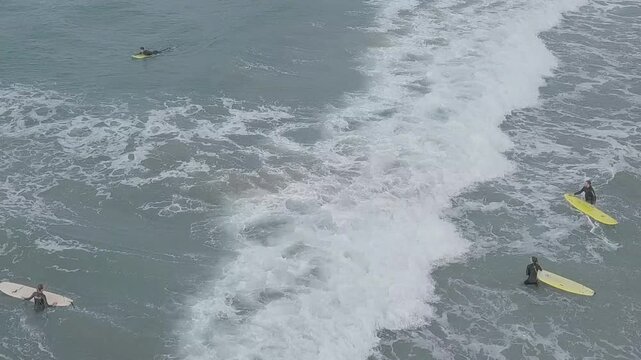 Surfers near a beach beneath volcanic cliffs