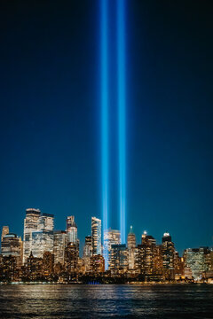 Blue light beams of Tribute in Light over Manhattan skyline at night. Tribute in Light two vertical searchlights beam into dark sky over illuminated buildings of downtown Manhattan.