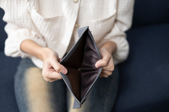 Financial hardship and empty wallet concept, showing a person opening an empty wallet while sitting at home, symbolizing limited income, money problems, and financial stress.