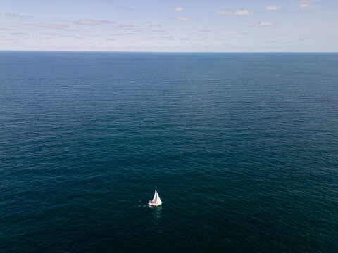 White Sailboat Sailing Alone on Open Blue Sea Ocean Horizon Aerial