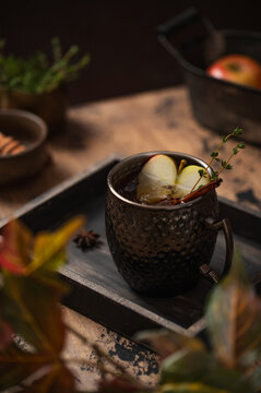 Apple cider with ice and thyme in hammered mug, moody autumn beverage