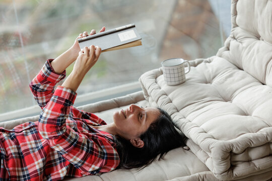 Smiling woman lying down reading a book with a cup of coffee beside her