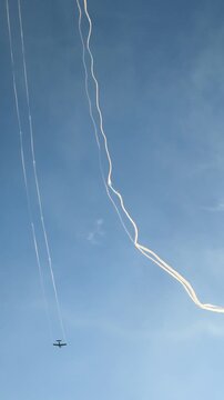 Spectacular aerobatics airshow performance with a stunt airplane flying high in a clear blue sky, leaving a white smoke trail and creating circular smoke rings during an outdoor summer aviation event.