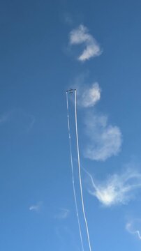 Spectacular aerobatics airshow performance with a stunt airplane flying high in a clear blue sky, leaving a white smoke trail and creating circular smoke rings during an outdoor summer aviation event.