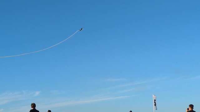 Spectacular aerobatics airshow performance with a stunt airplane flying high in a clear blue sky, leaving a white smoke trail and creating circular smoke rings during an outdoor summer aviation event.