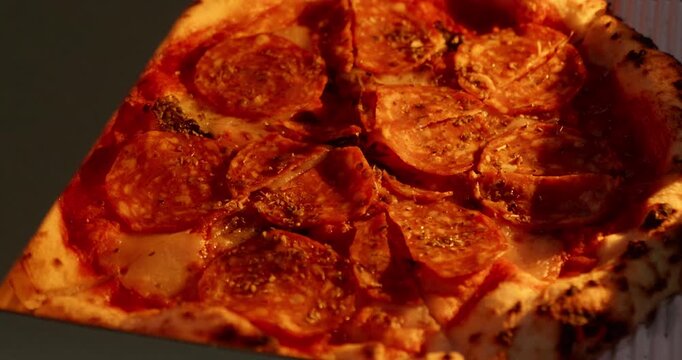 Close up shot of spicy salami pizza inside a delivery container. Warm golden light highlights the crispy charred crust and melted toppings.