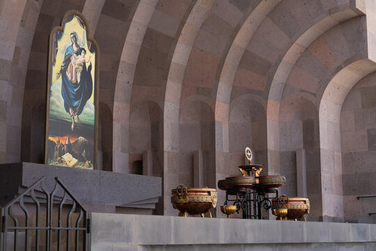 Interior of a monumental stone church featuring an altar, ornate ceremonial vessels, vaulted arches, and a colorful Madonna and Child religious panel. 