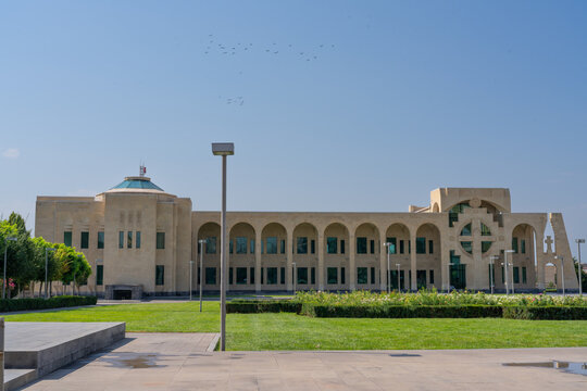 Large modern Christian church with arched windows, cross-shaped facade detail, green lawns and a paved courtyard on a clear sunny day. 