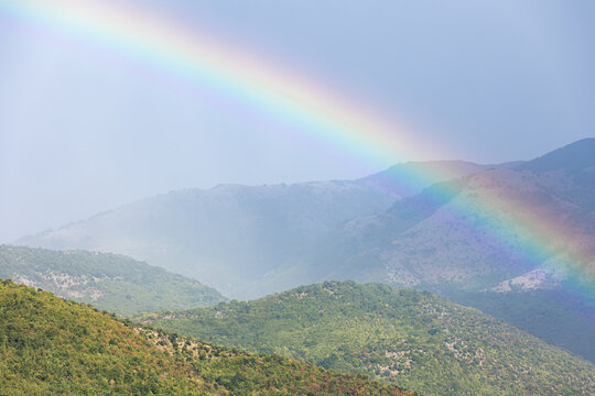 A brilliant rainbow arcs gracefully over lush green mountain peaks covered in soft mist. These magnificent weather phenomena inspire a profound sense of natural harmony, peaceful renewal and hope.