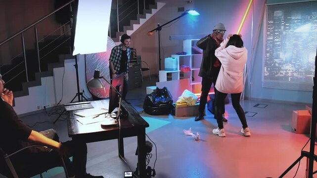 A group of casually dressed individuals interact around professional equipment in an industrial indoor studio setting during a film production.