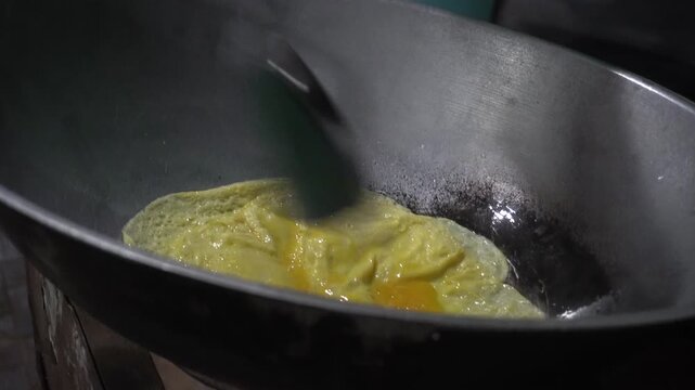 Close-up footage of golden fried egg cooking in tilted wok, homemade omelette sizzling in traditional kitchen pan.