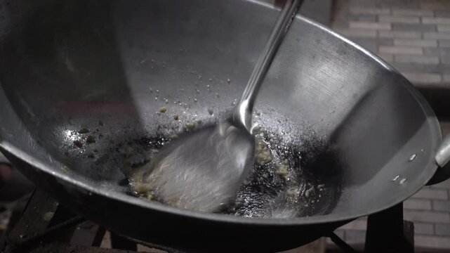 Close-up footage of stirring sizzling garlic and spices in hot wok with spatula.