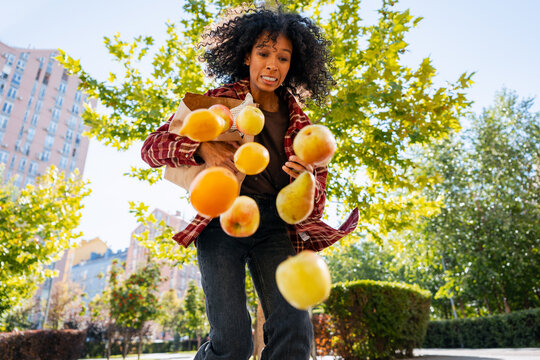 Young woman accidentally dropping fruit from grocery bag outdoors