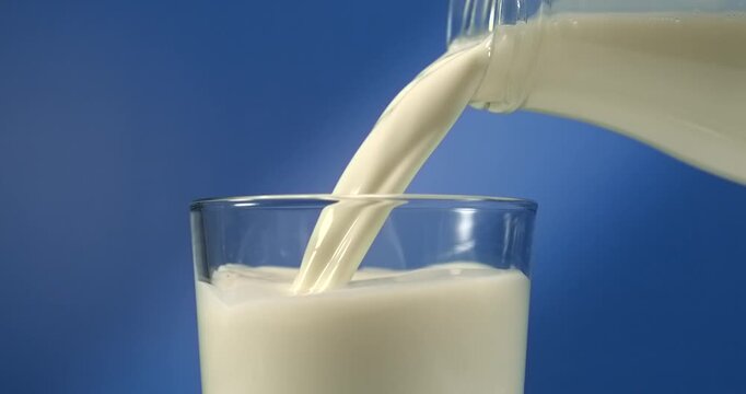 Milk pouring from bottle into glass on blue background in slow motion
