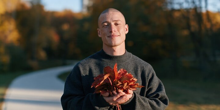 Portrait of a smiling bald man holding red autumn leaves in a park for fall background and seasonal banner design