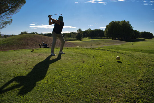 Golfer at the top of his backswing on the tee, building power before striking the ball, yellow tee markers visible nearby.