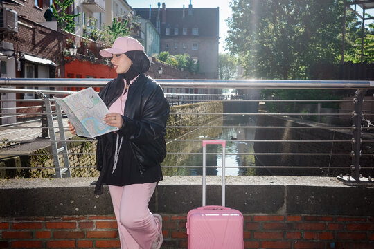 Woman with map and suitcase on canal bridge