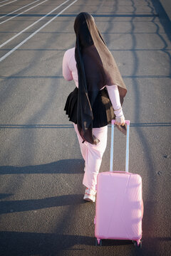 Woman with headscarf pulling pink suitcase across lot